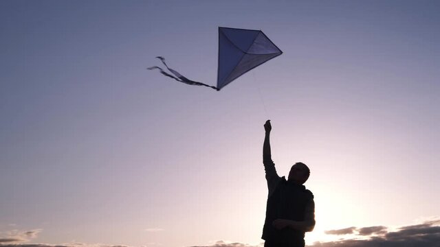 Blue kite soars in the sunset sky. Man rules kite. The concept of freedom, summer hobbies, entertainment in nature. Minimalism, space for text, shades of blue. Silhouette	