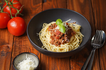 spaghetti with bolognese tomato sauce and fresh basil in black bowl on wooden table