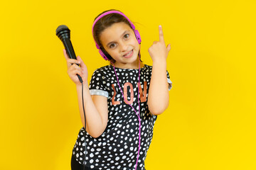 little pretty child listening music in headphones and singing isolated over yellow background