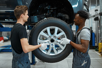 Fototapeta na wymiar Two male mechanics fixes wheel, car service