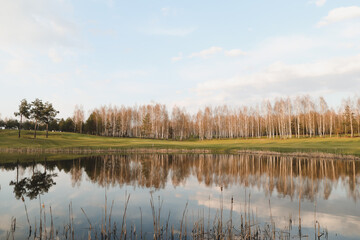 spring landscape, forest lake in spring surrounded by trees, calm water surface with reflection, bright sunlight and blue sky