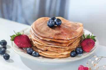 Stack of homemade delicious pancakes with forest fruits on a white plate, close up, macro photography
