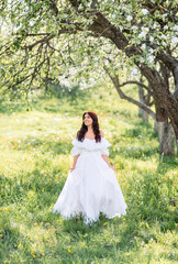 Obraz na płótnie Canvas Beautiful woman in a long white dress in a spring garden. A girl runs through a blooming garden.