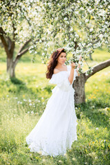 Obraz na płótnie Canvas Beautiful woman in a long white dress in a spring garden. A girl in a blooming garden.