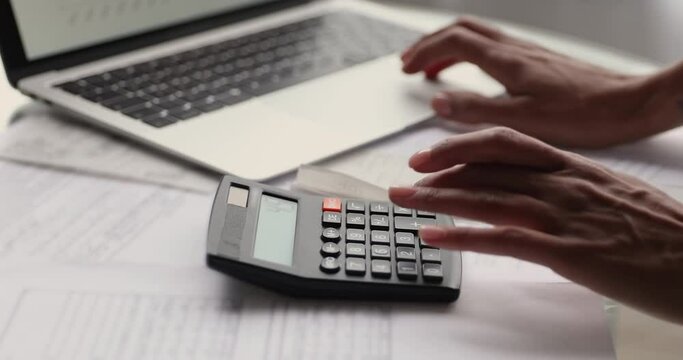Close up view African female hands using calculator calculates expenses, pay bills, taxes, loan through e-bank application on laptop. Personal finances management and control, accountancy job concept