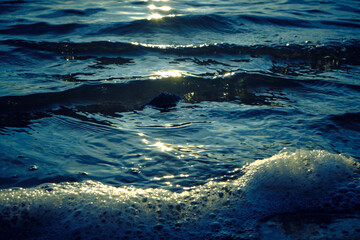 Waves and foam on the beach during sunset.