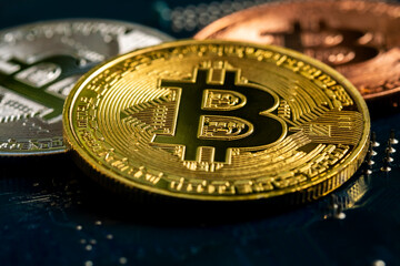 Macro view of gold, silver and bronze color shiny coins with bitcoin symbol on a mainboard.