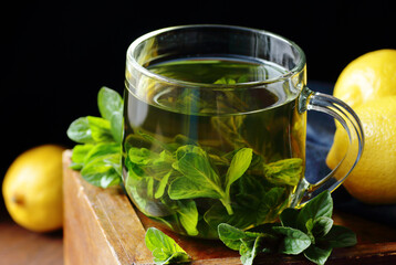 Mint herbal tea in a glass cup on dark moody wooden rustic background with blue linen napkin, closeup, copy space, natural medicine, naturopathy, drinks for sleep and energy concept