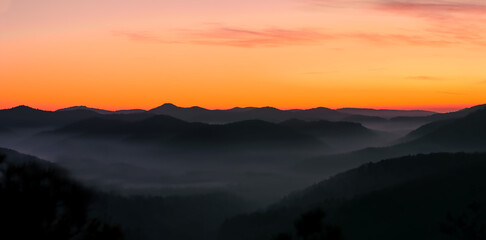 foggy, misty valley with orange sky before sunrise, beautiful orange yellow lighted sky