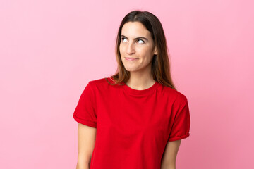 Young caucasian woman isolated on pink background having doubts while looking up