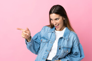 Young caucasian woman isolated on pink background pointing finger to the side and presenting a product