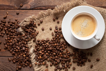 Cup of freshly brewed coffee on wooden table with roasted coffee beans on wooden background. View top