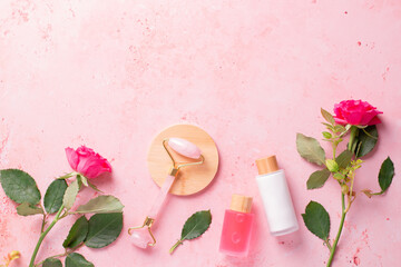 Rose extract natural cosmetics in reusable bottles with gua sha facial beauty roller and natural rose flowers on pink, border with copy space