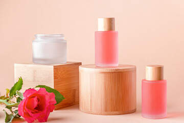 Rose extract natural cosmetics in reusable bottles and rose flower on wooden risers. Plant based, organic cosmetics still life