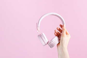 Woman hand holding pink headphones over pink background.