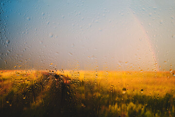 Road goes into distance background of a rainbow after rain view through wet in drops of glass.