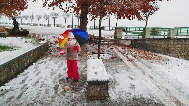 Little child girl with umbrella of many colors plays kicking snowball. Real time