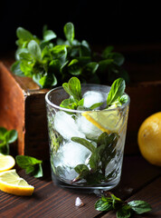 Mint with lemon citrus cocktail or mocktail with ice in glass on dark moody vintage wooden...