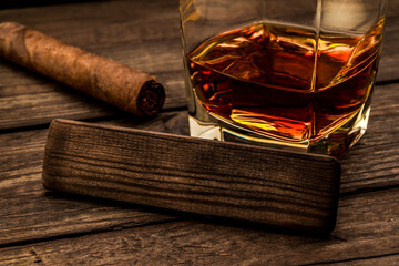 Glass of brandy with cuban cigar and the empty wooden plank on an old wooden table. Close up view,...