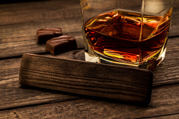 Glass of brandy with chocolate and the empty wooden plank on an old wooden table. Close up view,...
