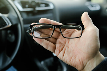 Car driver hand holding optical glasses on car interior background close up