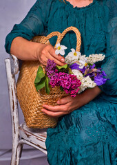 Woman holding hands wicker bag with lilac flowers indoor, Sitting on a vintage chair