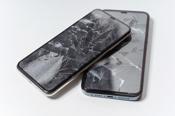 Two broken smartphones on a white background. Crash protective tempered glass for smartphone. A...