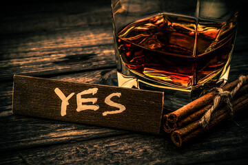 Glass of brandy with cinnamon sticks tied with jute rope and the wooden plank on it is an...