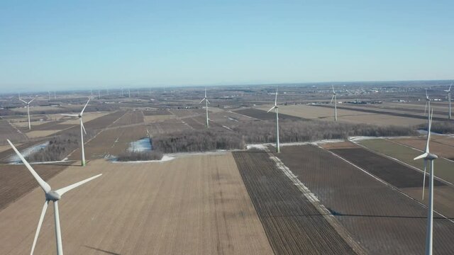 drone going back in a wind turbine field or wind farm in a sunny day, looking from high altitude in a sunny day