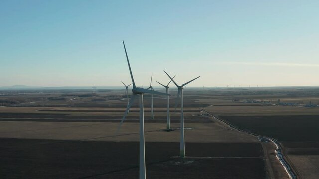 drone side move left to right looking the front of a wind farm turbines n the sun is back