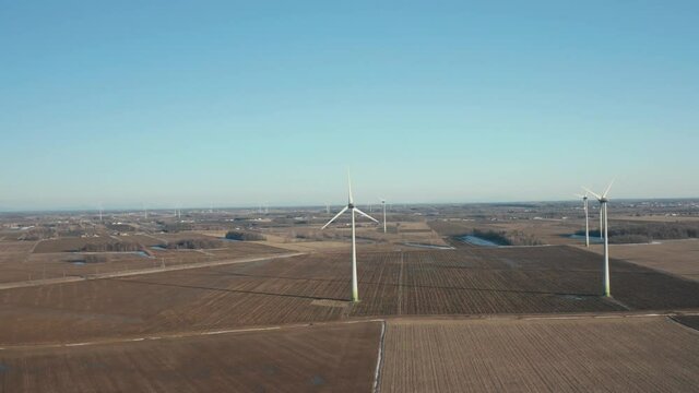 drone flying around a wind turbine farm with some cars passing by, showing the integration between us and them.