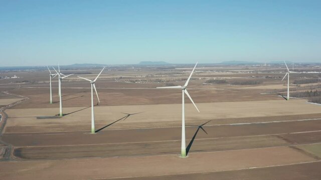 drone desending overlooking a wind farm with many turbines, a lot of them insde the shot, sunny day and begining of winter