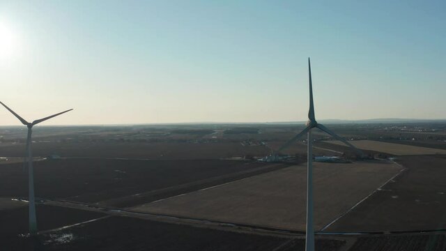 drone flying at the same height as the axis of some huge wind turbines with the sun in the back