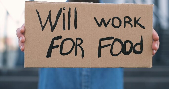 Close up of carton poster with words Will work for food in male hands outdoor. Caucasian workless man holding table with unemployment slogan.