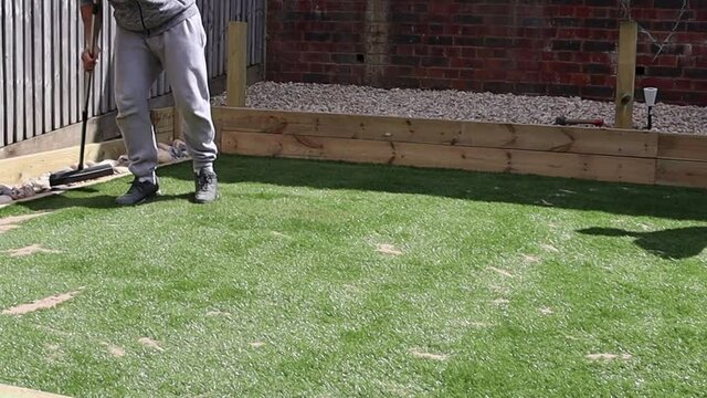 Man sweeping sand into artificial grass