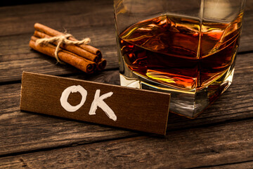 Glass of brandy with cinnamon sticks tied with jute rope and the wooden plank on it is an inscription 