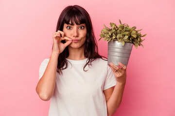 Young caucasian woman holding a plant isolated on pink background with fingers on lips keeping a...