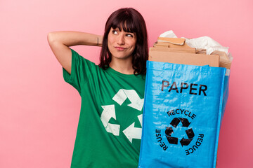 Young caucasian woman holding a recycled cardboard bag isolated on pink background touching back of head, thinking and making a choice.