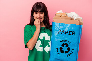 Young caucasian woman holding a recycled cardboard bag isolated on pink background biting fingernails, nervous and very anxious.