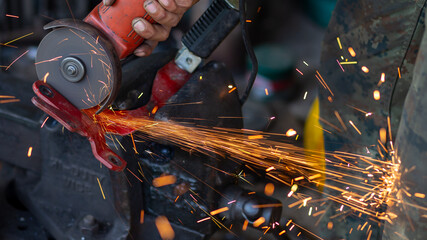 Young workers use metal grinders Steel parts of a motorbike To design and modify Beautiful orange sparkle from metal grinding.