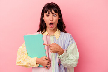 Young student caucasian woman holding books isolated on pink background pointing to the side