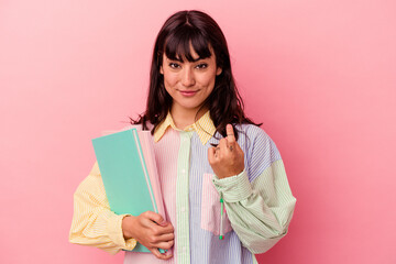 Young student caucasian woman holding books isolated on pink background pointing with finger at you as if inviting come closer.