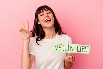 Young caucasian woman holding a vegan life placard isolated on pink background joyful and carefree...