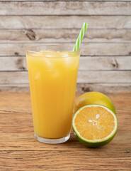Orange juice in a glass with ice and fruits over wooden table