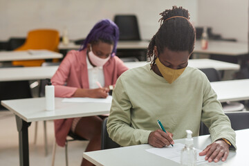 Portrait of young African-American man wearing mask while taking test or exam in school with hand sanitizer, copy space