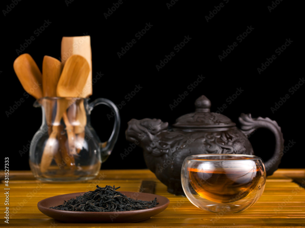 Wall mural Chinese tea ceremony. Clay teapot with red tea Lapsang souchong on a black background and glass thermo cup of hot tea.