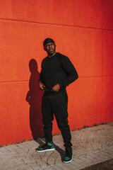 Chico negro apuesto con bandana en la cabeza y vestido de negro posando delante de una pared roja