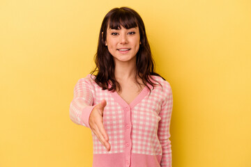 Young caucasian woman isolated on yellow background stretching hand at camera in greeting gesture.