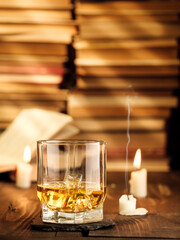 A glass of whiskey on the table with books and burning candles. Copy space, vertical photo.