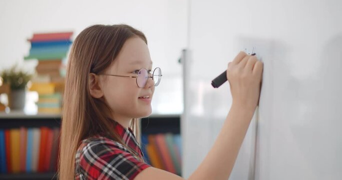 Child writing solution of mathematical operation on board in classroom.
